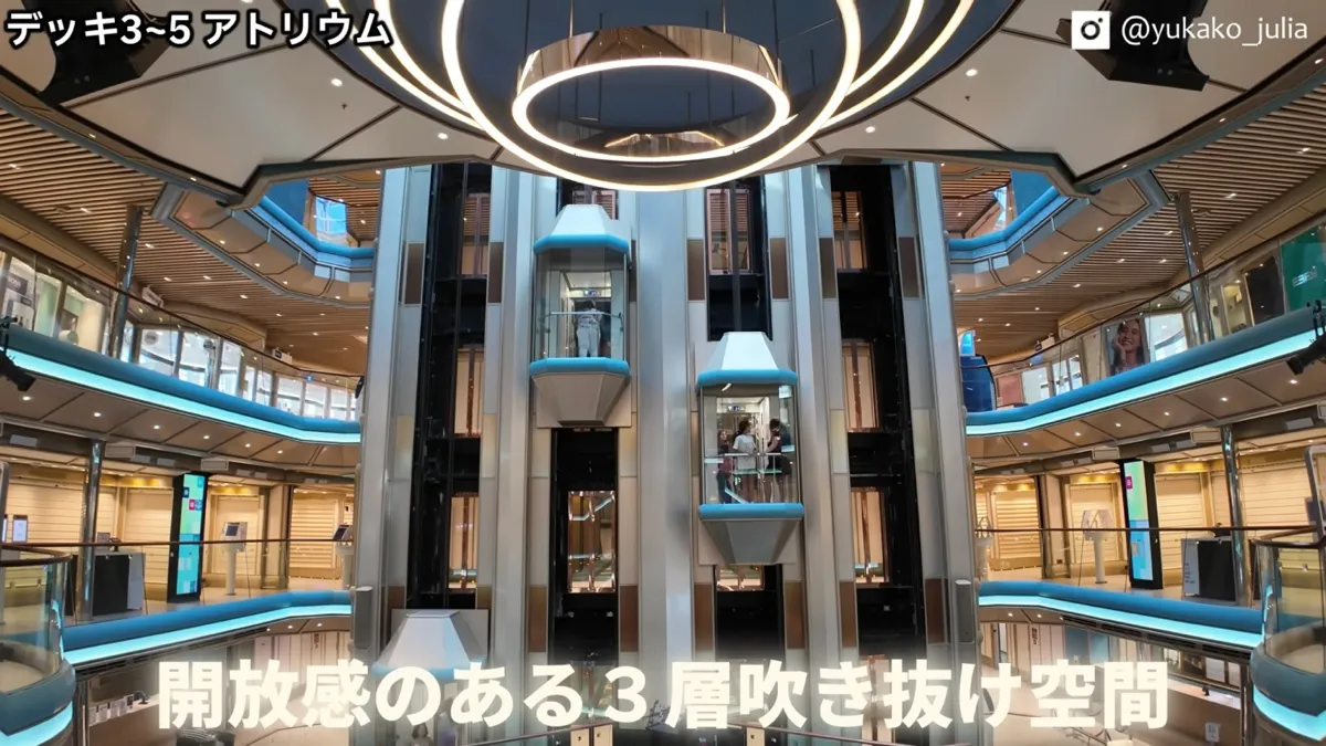 デッキ3〜5の3層吹き抜けのアトリウム。ガラス張りのエレベーターと円形の照明
